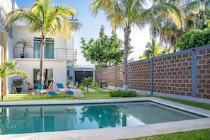 Ein moderner Poolbereich mit rechteckigem Pool, Liegestühlen und Palmen.