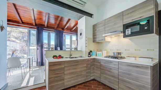 A modern kitchen with wooden cabinets, a built-in microwave, and a large window overlooking a patio area. - Stella Del Lago Pied Dans L'eau in Arona (Arona)