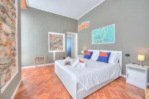 A bedroom with a bed, a nightstand, a wall-mounted artwork, a small table, and a brick wall.