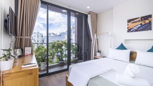 Habitación de hotel con cama, escritorio con computadora, televisión y balcón con plantas en macetas.
