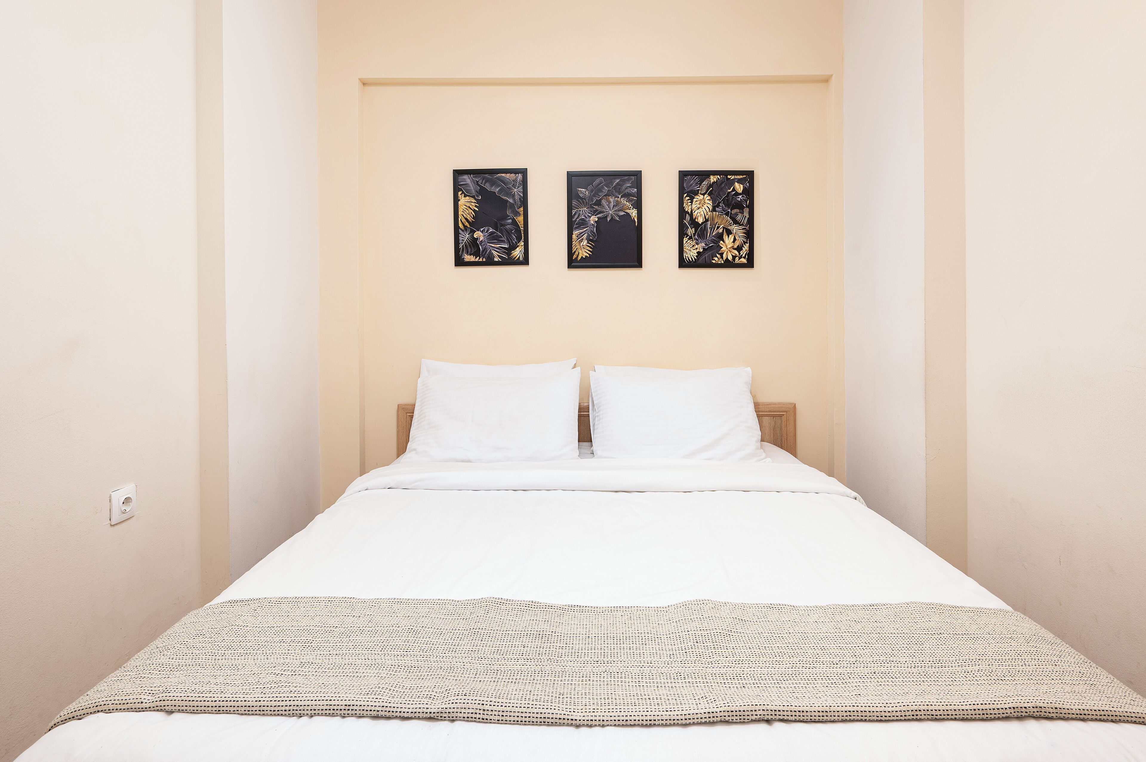 A bedroom with a bed, white bedding, a beige wall, and three framed pictures above the bed.