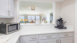A modern kitchen with white cabinets, a microwave, a coffee maker, and a view of a balcony with a railing and a lamp. - Stunning View- Low Density Complex (Gulf Shores)