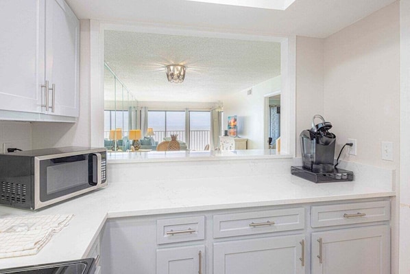 A modern kitchen with white cabinets, a microwave, a coffee maker, and a view of a balcony with a railing and a lamp. - Stunning View- Low Density Complex (Gulf Shores)