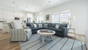 A modern living room with a grey sectional sofa, a striped armchair, and a round coffee table. - Lost Dunes Cottage- Walking Distance to Beach! (Gulf Shores)