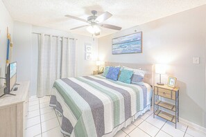 A bedroom with a bed, a ceiling fan, a nightstand with a lamp, a TV, and a window with curtains. - Gulf Front Condo with a Gorgeous View (Orange Beach)