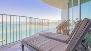 A balcony with a view of the sea, two lounge chairs, and a small table.