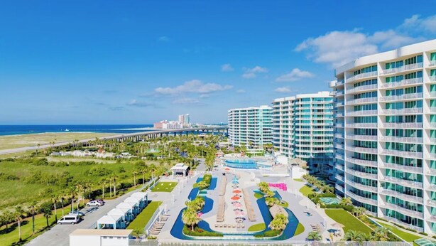 A hotel with a pool, a beach view, and a parking area.