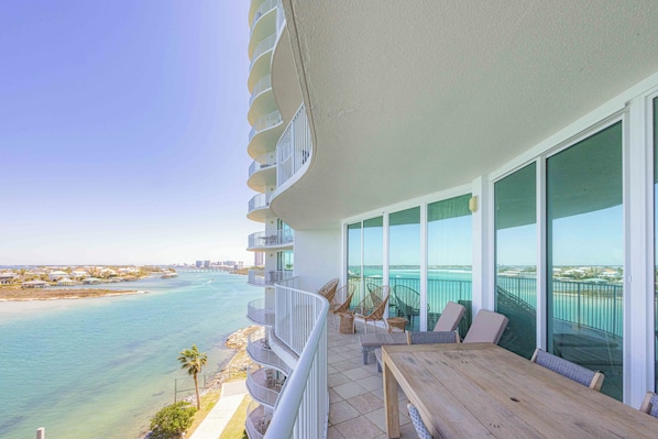 A balcony with a view of the ocean, wicker chairs, and a wooden table.
