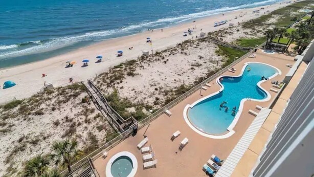 A beach resort with a pool, beach umbrellas, and lounge chairs.
