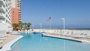 A swimming pool with lounge chairs and an American flag, surrounded by buildings and a clear sky.