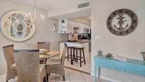 A dining area with wicker chairs, a chandelier, and a round mirror on the wall.
