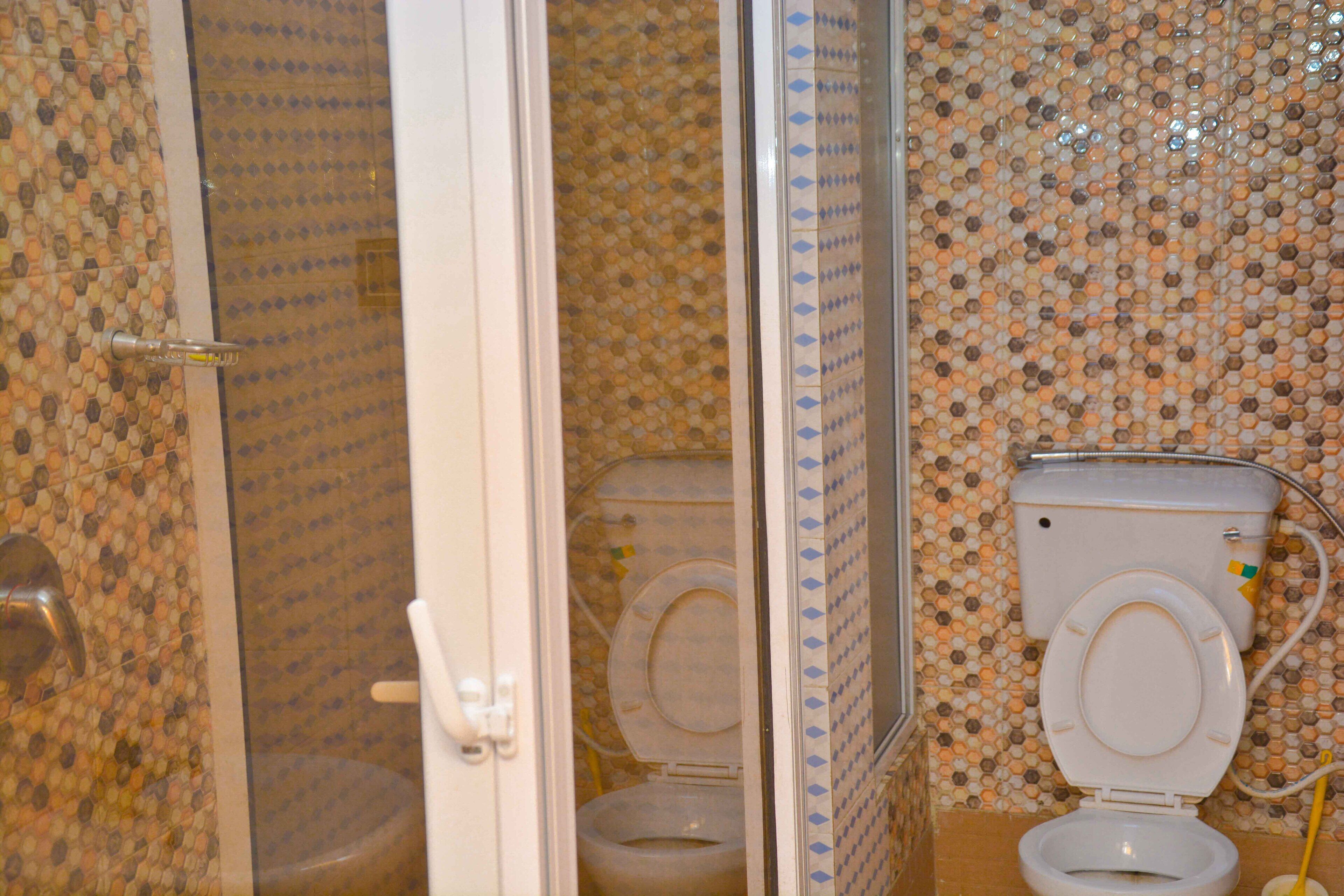 A bathroom with two toilets, a shower, and a tiled wall.