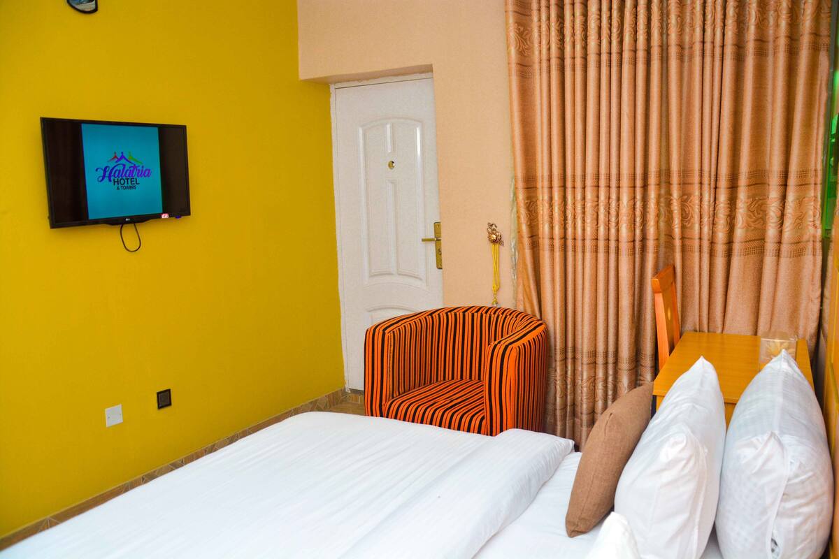 A hotel room with a bed, a TV mounted on the wall, a door, and curtains.