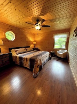 Relax in this inviting bedroom with a large bed and ceiling fan, featuring a bedside table and lamp.