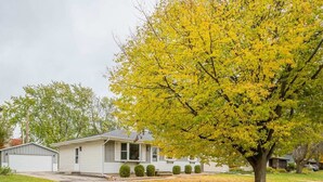 Une maison de plain-pied avec un garage, une pelouse et un arbre aux feuilles jaunes.