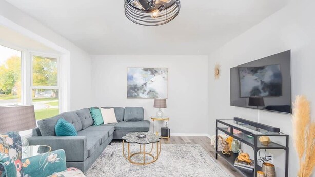Un salon moderne avec un canapé gris, une table basse ronde et un téléviseur fixé au mur.