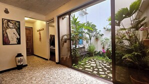 A hallway with a tiled floor, a wooden door, a bench, and a glass door leading to a garden with plants and a stone pathway.