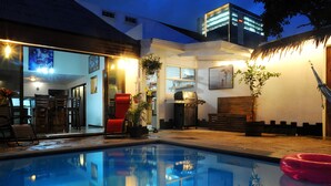 A swimming pool with a red float, a barbecue area, and a dining space with chairs and a table.