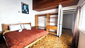 Une chambre à coucher avec un lit en bois, une armoire dont les portes sont ouvertes et un parquet à motifs en chevrons.