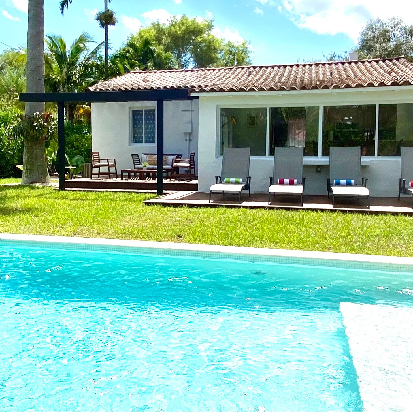 Une maison avec une piscine, un patio couvert avec des chaises et un jardin.