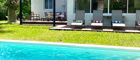 Una casa con piscina, un porche cubierto con sillas y un jardín.