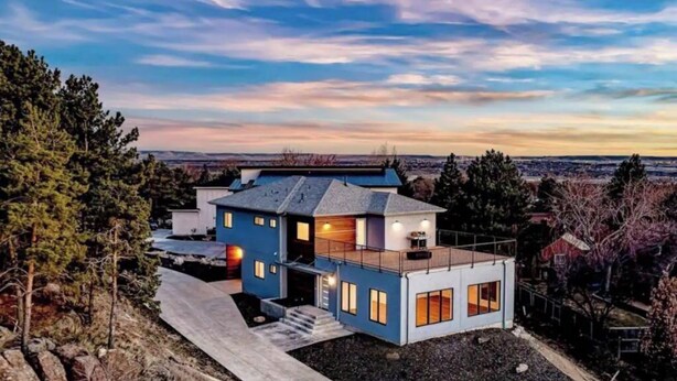 Una casa moderna de dos pisos con techo plano, ventanas grandes y base de piedra.