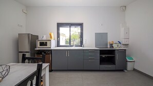 A modern kitchen with grey cabinets, a microwave, a refrigerator, and a window with a view of the outside. - Little House - GARDEN - GRAULHET (Graulhet)