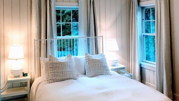 A bedroom with a bed, two bedside tables with lamps, a ceiling fan, and two windows with curtains. - Designer East Hampton Farmhouse - Bike to Amagansett, EH & Ocean Beaches, Pool (East Hampton)