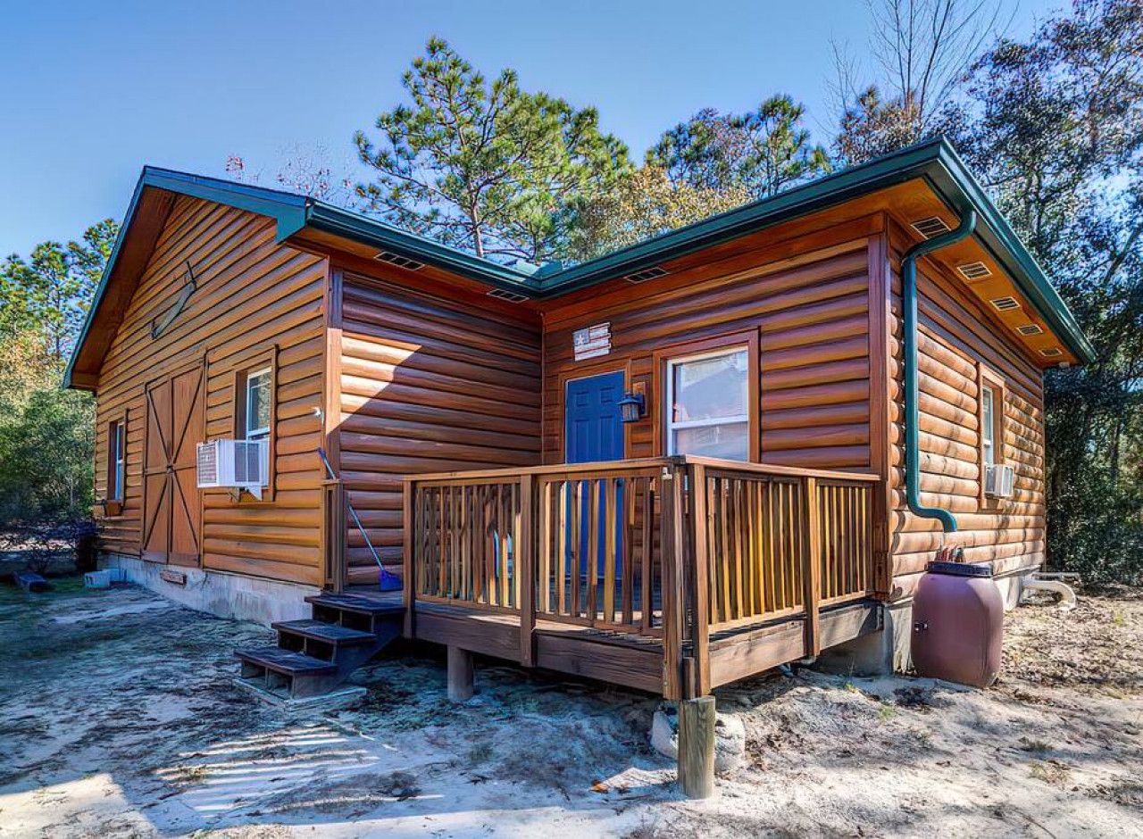A log cabin with a wooden deck, a front door, and a small window.