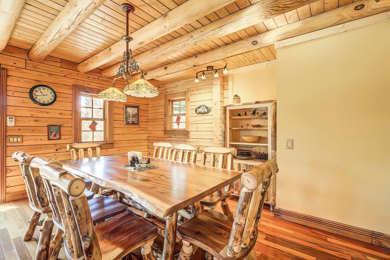 Une salle à manger rustique avec une table et des chaises en bois, un lustre et des murs en bois.