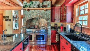 A kitchen with a stone fireplace, red cabinets, and a granite countertop.