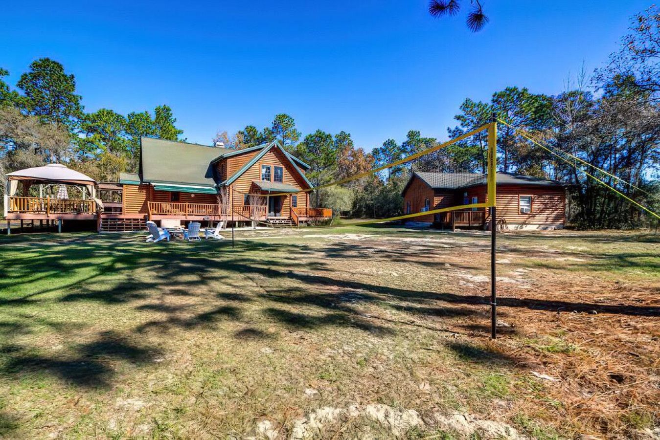 A cabin with a deck and a covered area, surrounded by trees and a clear sky.