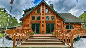A log cabin with a steeply pitched roof, a front porch with wooden railings, and a flagpole to the left.