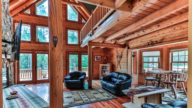 A spacious log cabin with a loft bedroom, large windows, and a cozy living area with a fireplace.