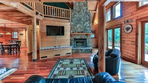 A log cabin interior with a stone fireplace, wooden furniture, and a balcony.