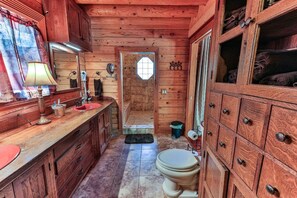 A wooden cabin bathroom with a sink, mirror, toilet, and cabinets. - Main Cabin & Bunkroom-HOT TUB, Grill, Fire Pit (Homosassa)