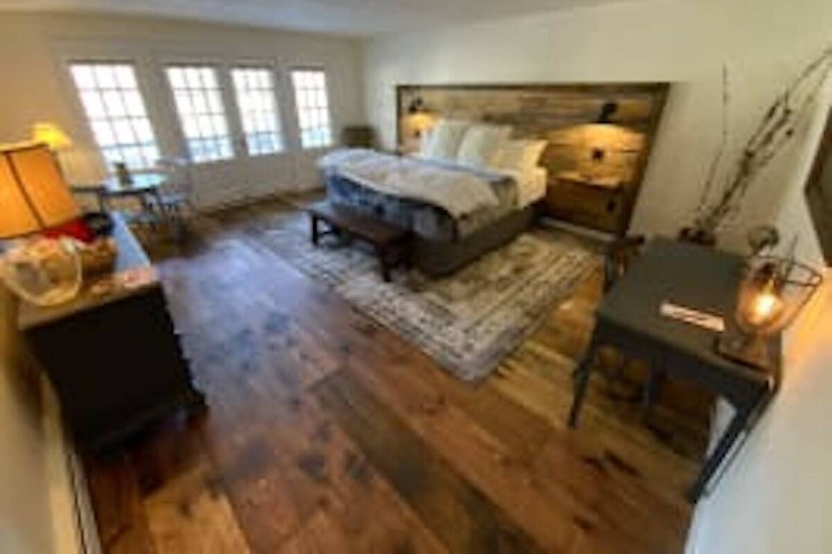 A spacious bedroom with a large bed, wooden flooring, a nightstand, and a bedside table with a lamp.
