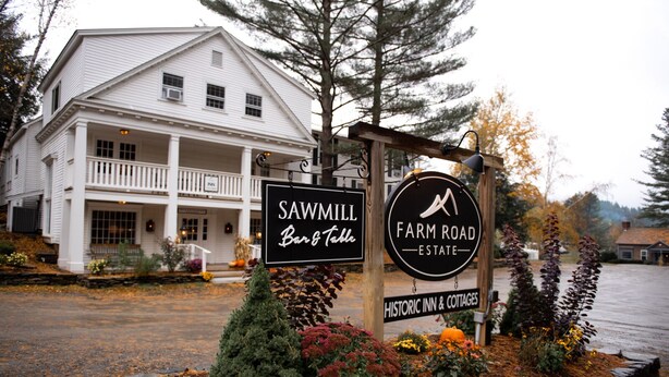A historic building with a porch, signs for 'Sawmill Bar & Table' and 'Farm Road Estate Historic Inn & Cottages'. - Farm Road Estate (West Dover)
