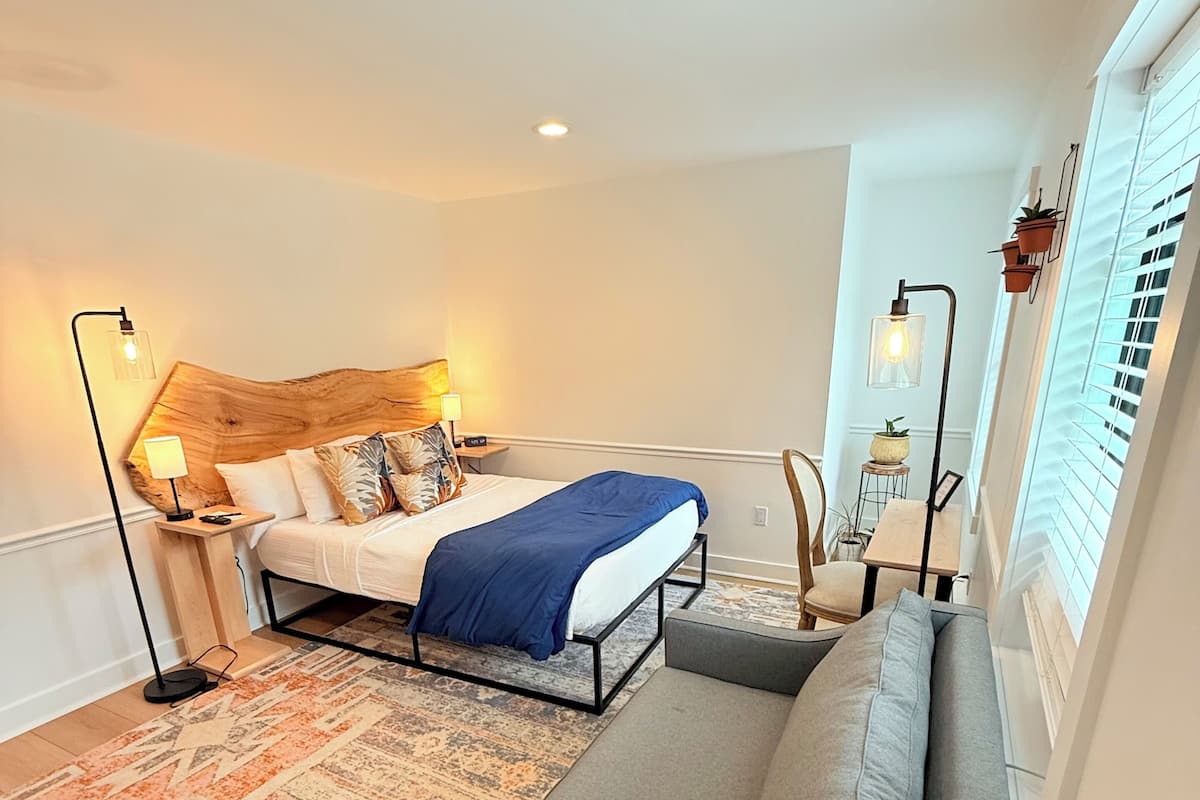 A modern bedroom with a wooden headboard bed, a grey sofa, a patterned rug, and two bedside lamps.