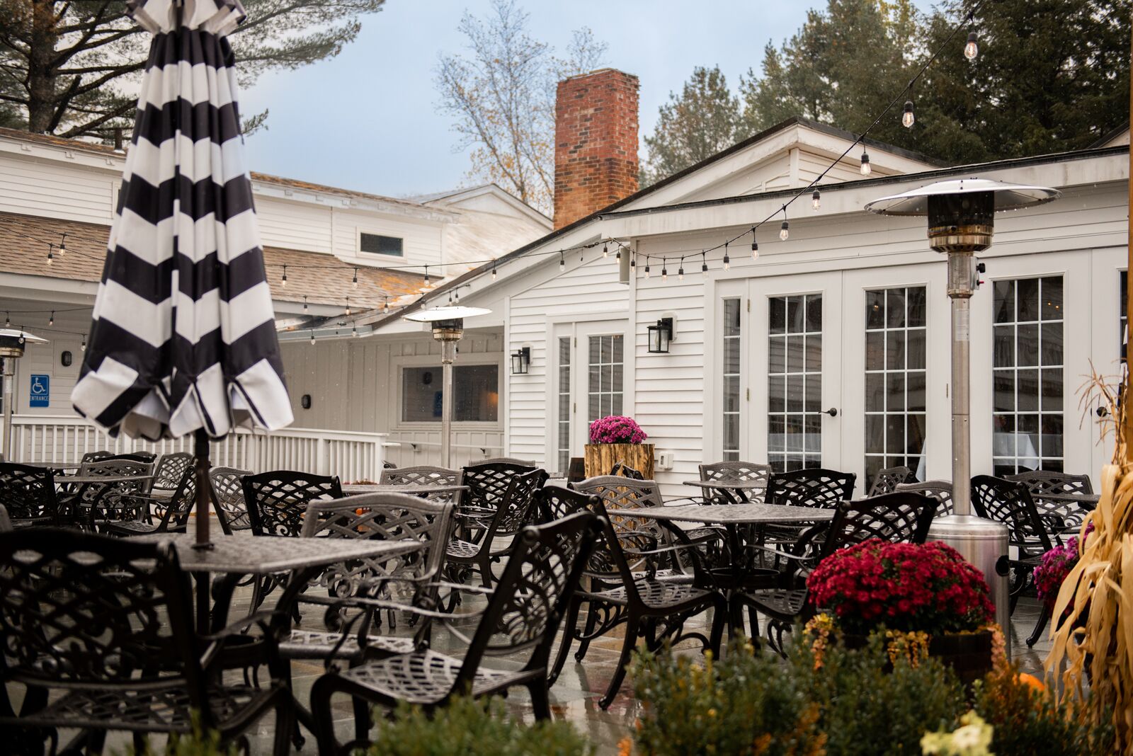 An outdoor patio with tables and chairs, a striped umbrella, and a brick chimney in the background.