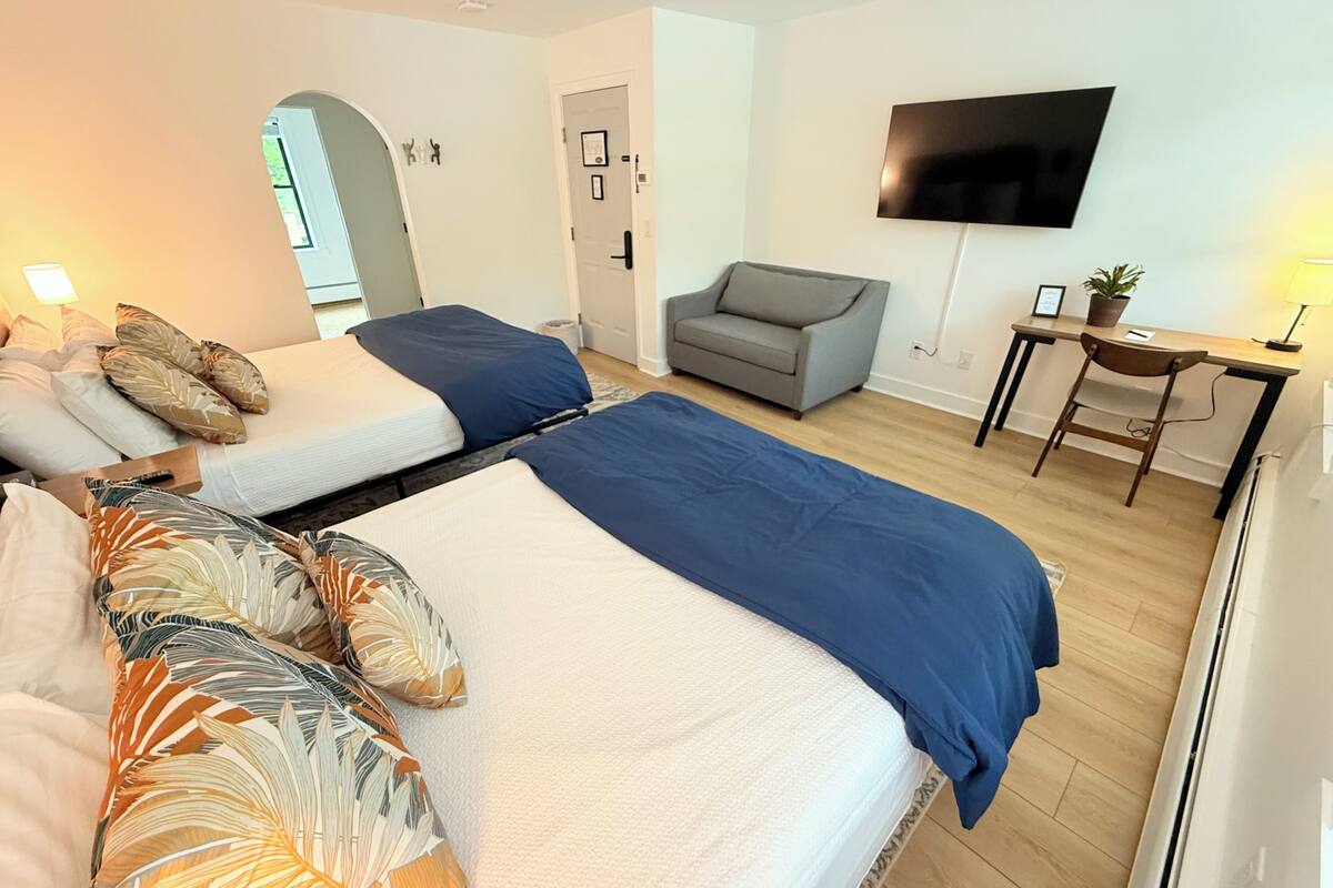 A hotel room with two beds, a sofa, a TV, a desk, and a chair.