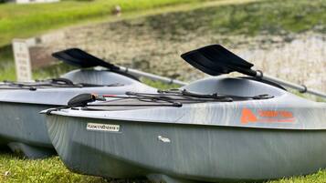 Two gray kayaks with 'OZARKTRAIL OUTDOOR EQUIPMENT' branding, parked on grass near a body of water.