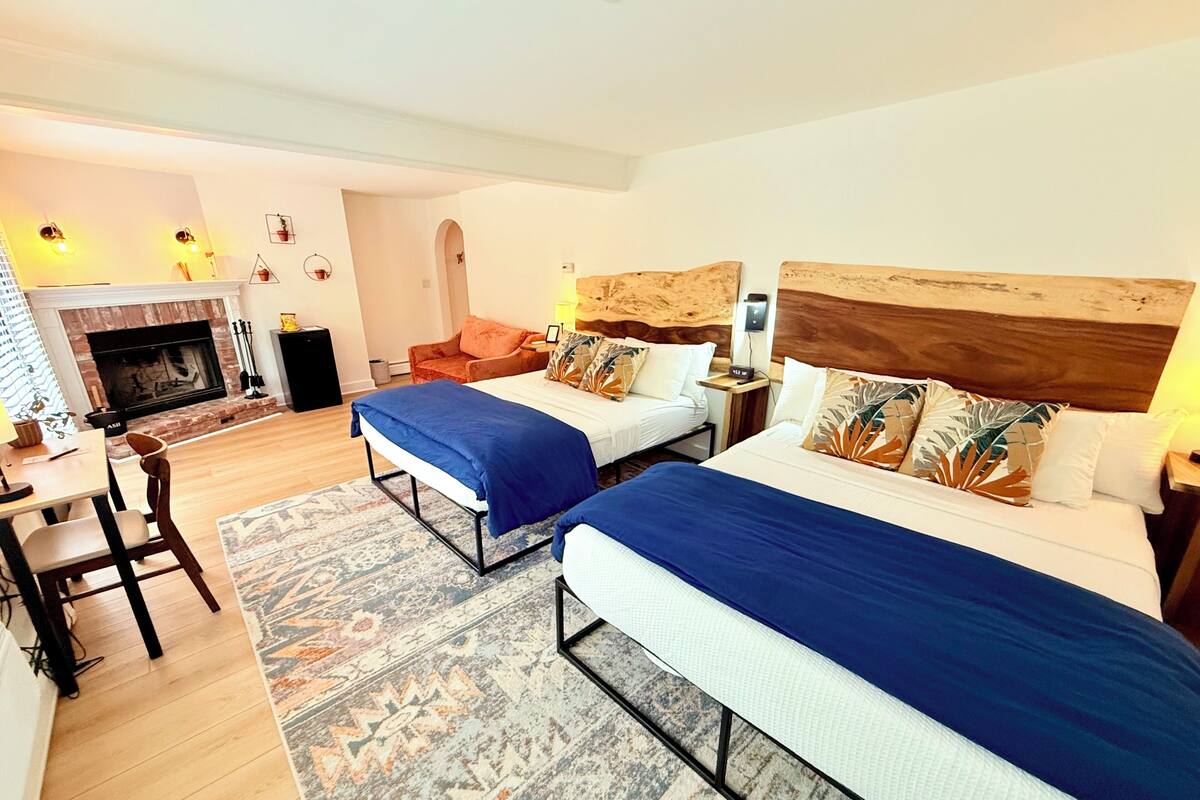 A hotel room with two beds, a fireplace, a dining area, and a small seating space.