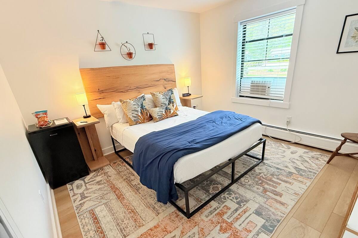 A modern bedroom with a bed, bedside tables, a heater, a window with blinds, and a small table with a bag of chips.