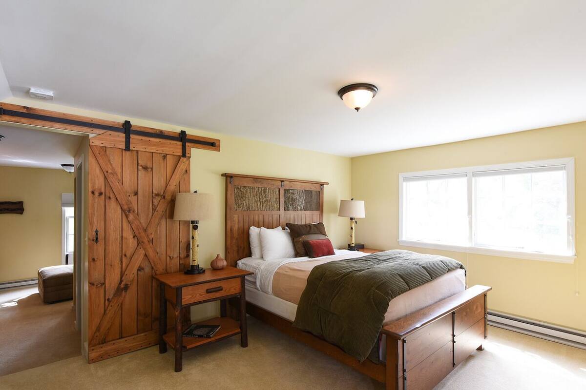 A bedroom with a bed, bedside tables, a wooden headboard, and a window.