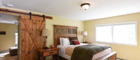 A bedroom with a bed, bedside tables, a wooden headboard, and a window.