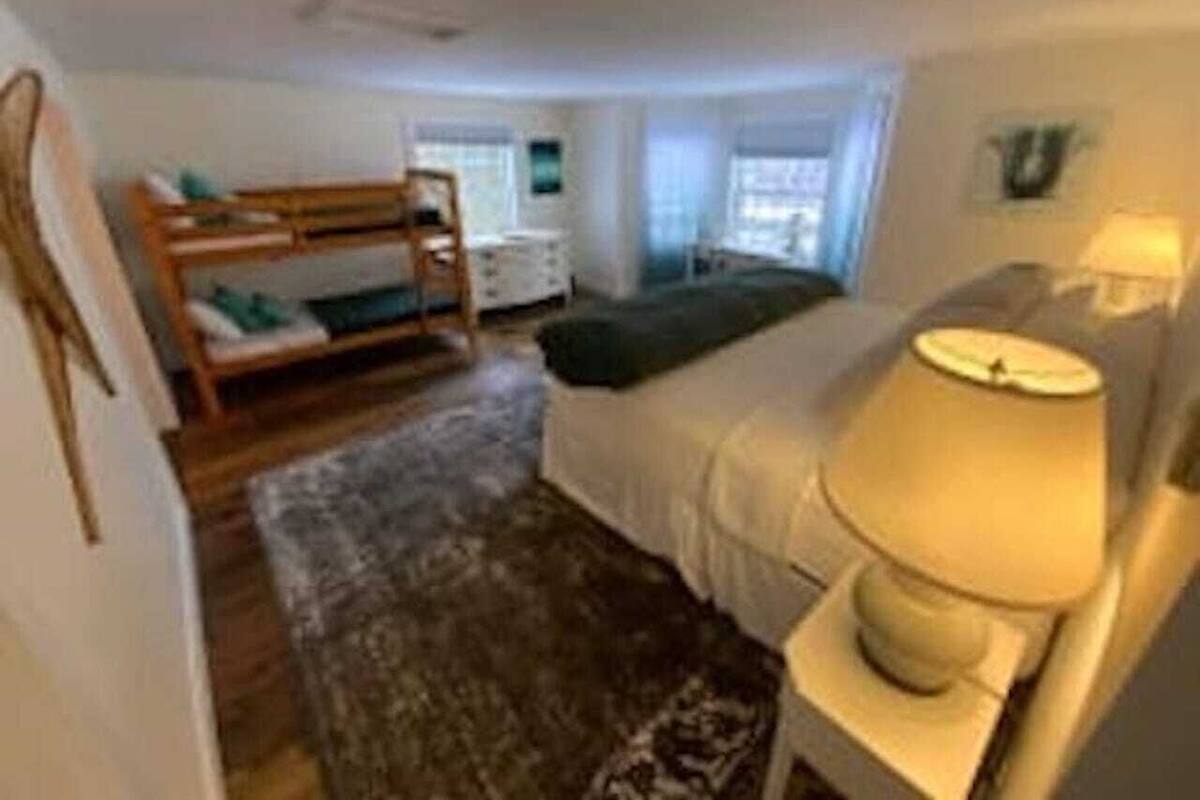 A bedroom with a bunk bed, a bedside table with a lamp, a dresser, and a window with curtains.