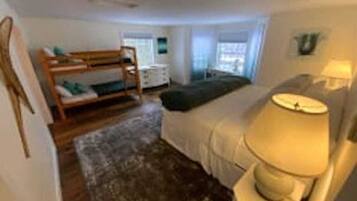 A bedroom with a bunk bed, a bedside table with a lamp, a dresser, and a window with curtains.