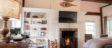 A cozy room with a fireplace, wooden beams, a bookshelf, and a television.
