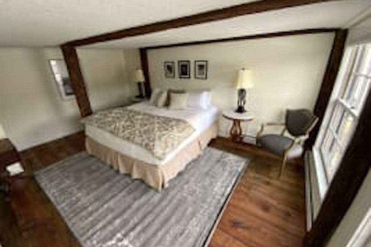 A bedroom with a large bed, a bedside table, a chair, and a window.